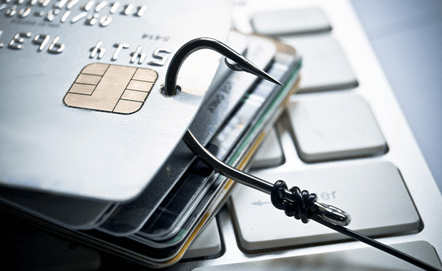 A fishhook piercing several credit cards placed on a computer keyboard.