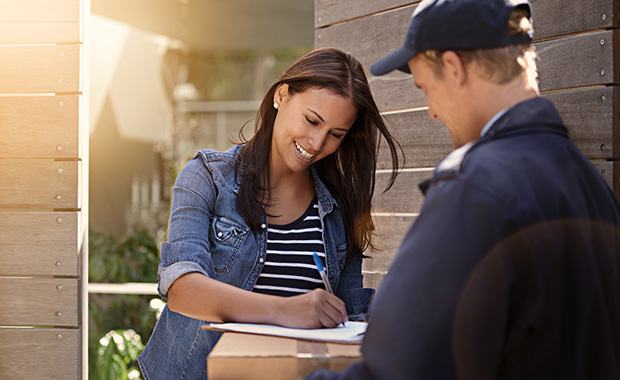 Smiling woman stands in doorway and accepts package from deliveryman