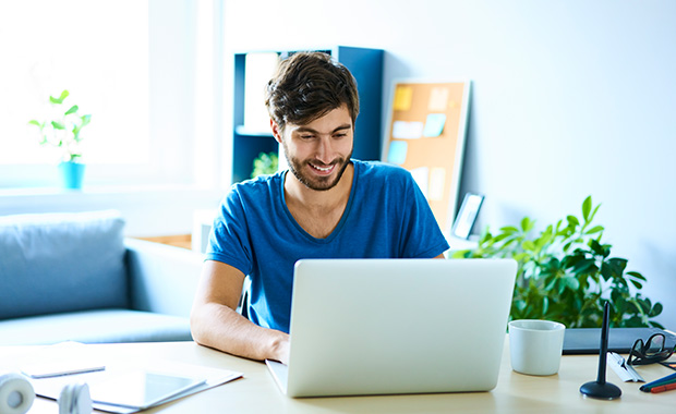 Young man working on laptop in home office and smiling