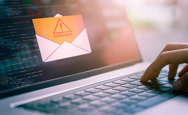 A hand typing on the keyboard of a laptop with a malware warning on the screen