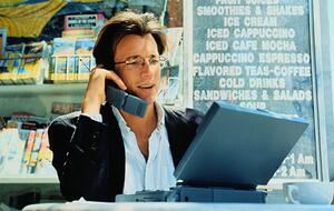 Man sits in caf&eacute; working on laptop and speaking on cell phone. The devices date the scene to the late 1990s