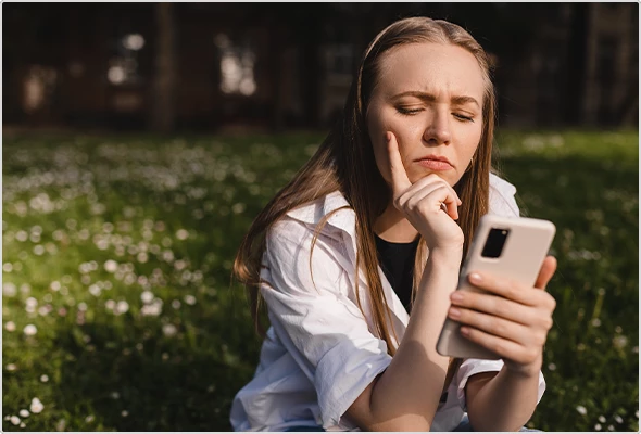 Woman sitting outside, looking puzzled at her smartphone.
