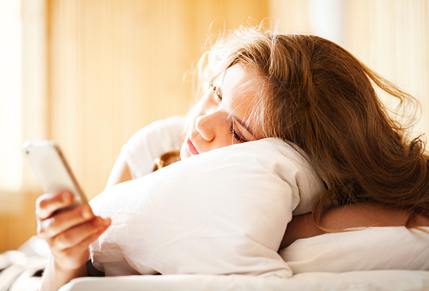 Sleepy woman lying in bed looking at phone